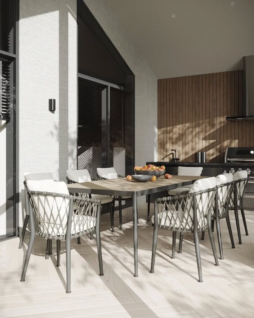 Bright and airy patio dining space with a modern wooden table, woven-cushioned chairs, and a sleek outdoor kitchen against a backdrop of vertical wooden slats.
